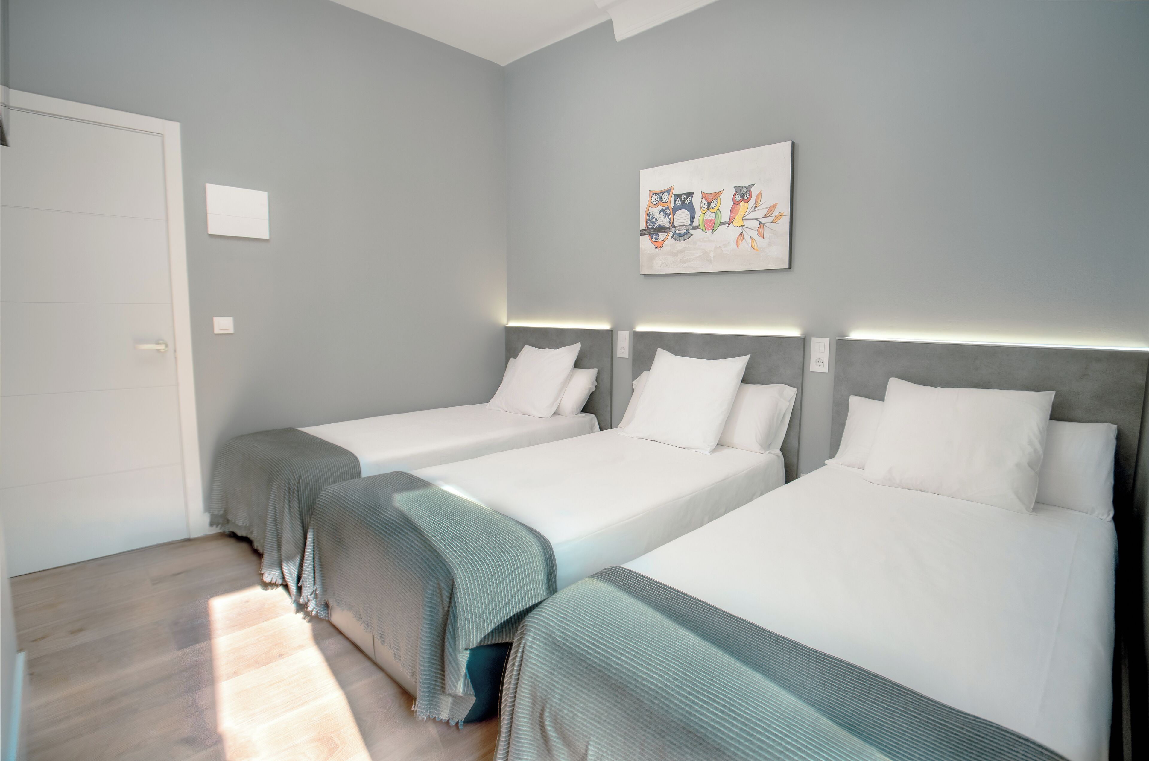 A hotel room with two beds, a door, a wall-mounted artwork, and a light switch.