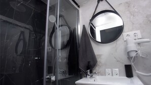 Un baño con cabina de ducha de vidrio, un lavamanos blanco con espejo y una toalla colgada en la pared.