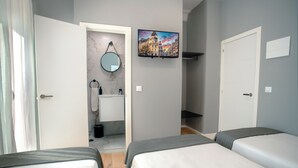 Habitación de hotel con dos camas, baño con espejo y lavamanos, y televisor en la pared.