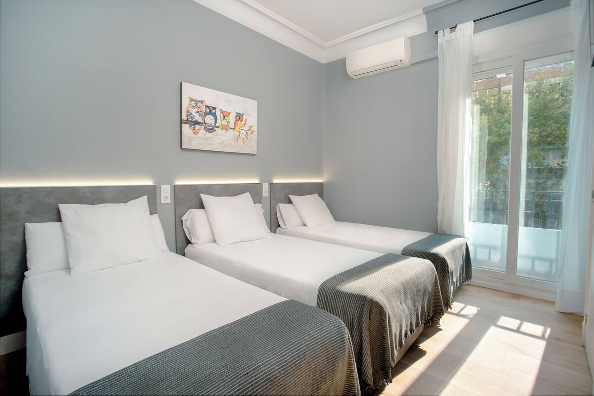 Habitación de hotel con dos camas, un ventanal con cortinas y un aire acondicionado instalado en la pared.