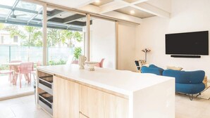 Une cuisine moderne avec un îlot central, un coin repas avec des chaises roses, un canapé bleu et un téléviseur fixé au mur.