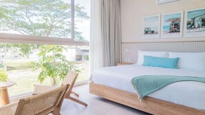 Une chambre avec une grande fenêtre, un lit avec un cadre en bois, une chaise et une petite table.