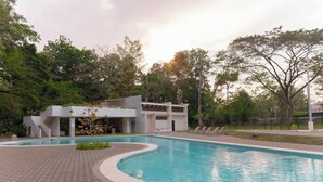 Une piscine à bord incurvé, entourée d’une zone pavée et d’un bâtiment à l’architecture moderne.