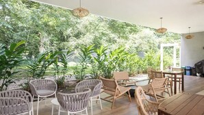 Un espace intérieur aménagé avec des meubles en osier, une table en bois et une vue sur la verdure grâce à une grande fenêtre.