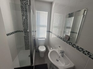 A bathroom with a glass shower enclosure, a toilet, a sink, and a mirror. - Cozy and Convenient Raynes Park maisonette (Greater London)