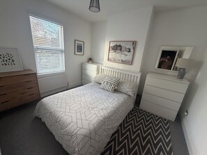 A bedroom with a bed, dresser, nightstand, and a window with blinds. - Cozy and Convenient Raynes Park maisonette (Greater London)