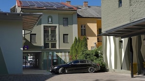 A building with a solar panel roof, a parked car, and a small tree in front.