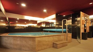 A modern indoor swimming pool with a clear water surface, surrounded by a stone wall and a wooden bench.