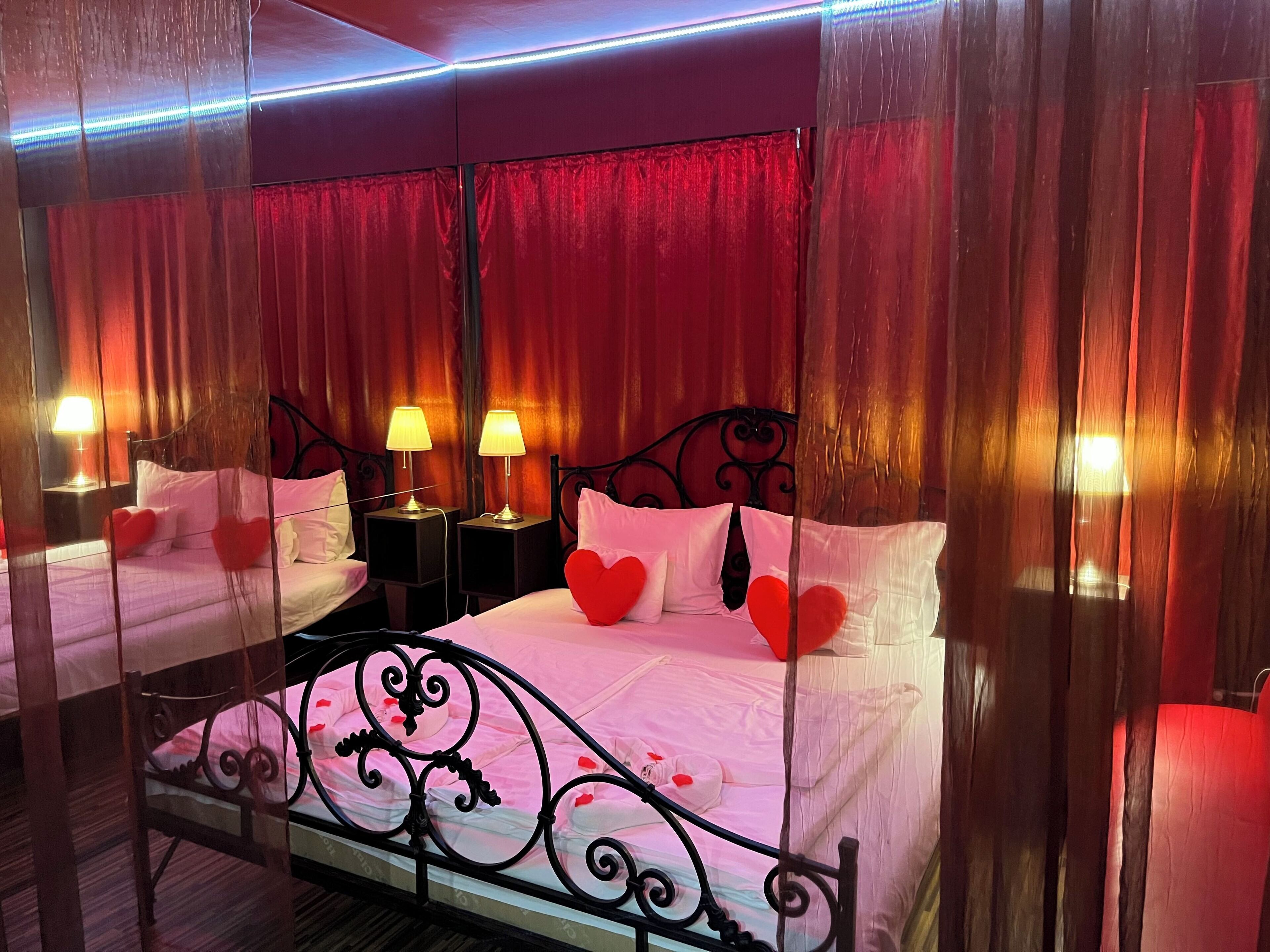 A double bed with a canopy, two bedside tables with lamps, and red heart decorations.