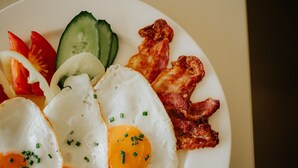 A plate with two sunny-side-up eggs, bacon, cucumber slices, and tomato slices.