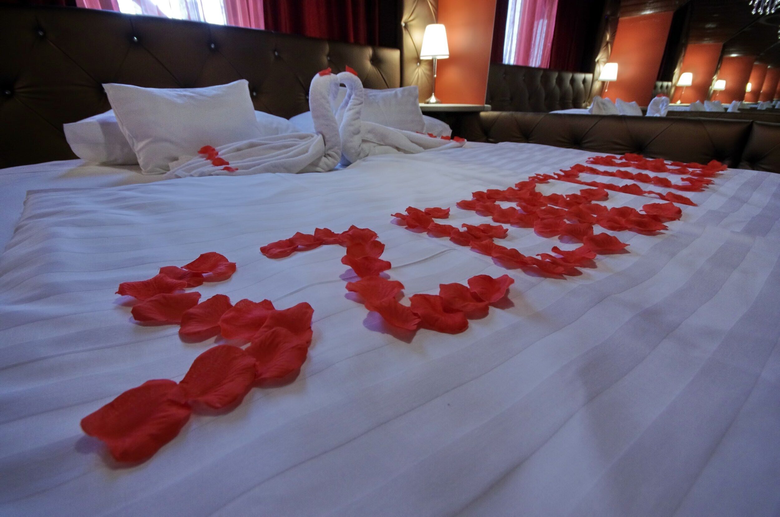 Una cama bien hecha con sábanas blancas y pétalos de rosa roja decorando el lecho.