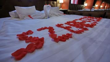 Una cama bien hecha con sábanas blancas y pétalos de rosa roja decorando el lecho.