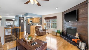 A spacious living room with a wooden coffee table, a fireplace, and a TV mounted on the wall. - Premiere Pointe with Golf Discounts (Branson)