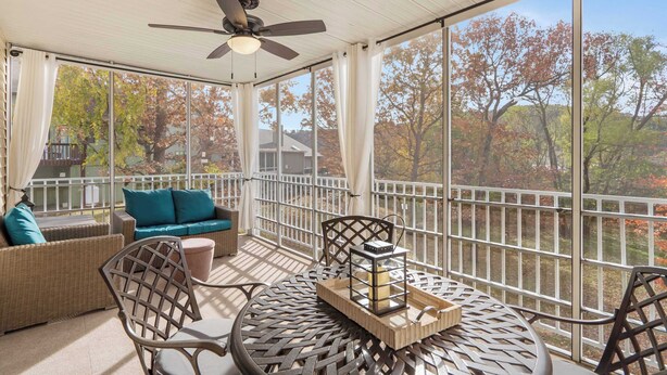 A covered patio with wicker furniture, a ceiling fan, and a view of autumn trees. - Premiere Pointe with Golf Discounts (Branson)