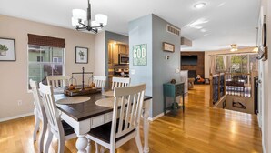 A spacious dining area with a wooden table and white chairs, a kitchen in the background, and a staircase leading to an upper level. - Premiere Pointe with Golf Discounts (Branson)