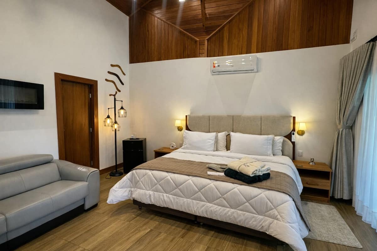 Ein Hotelzimmer mit einem Bett, einer Couch, einer Stehlampe, einem Fernseher und einer Klimaanlage.