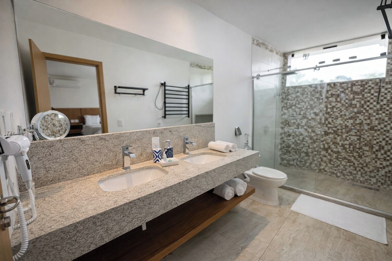 Uma casa de banho moderna com duas lavatórios, um espelho grande, um chuveiro com porta de vidro e um porta-toalhas.