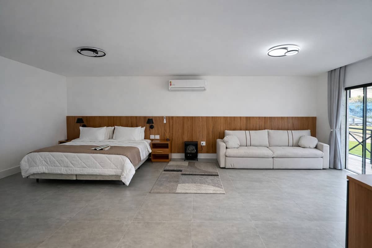 Ein modernes Hotelzimmer mit Bett, Sofa, einem Holz-Kopfteil, einer Klimaanlage und Blick ins Freie.