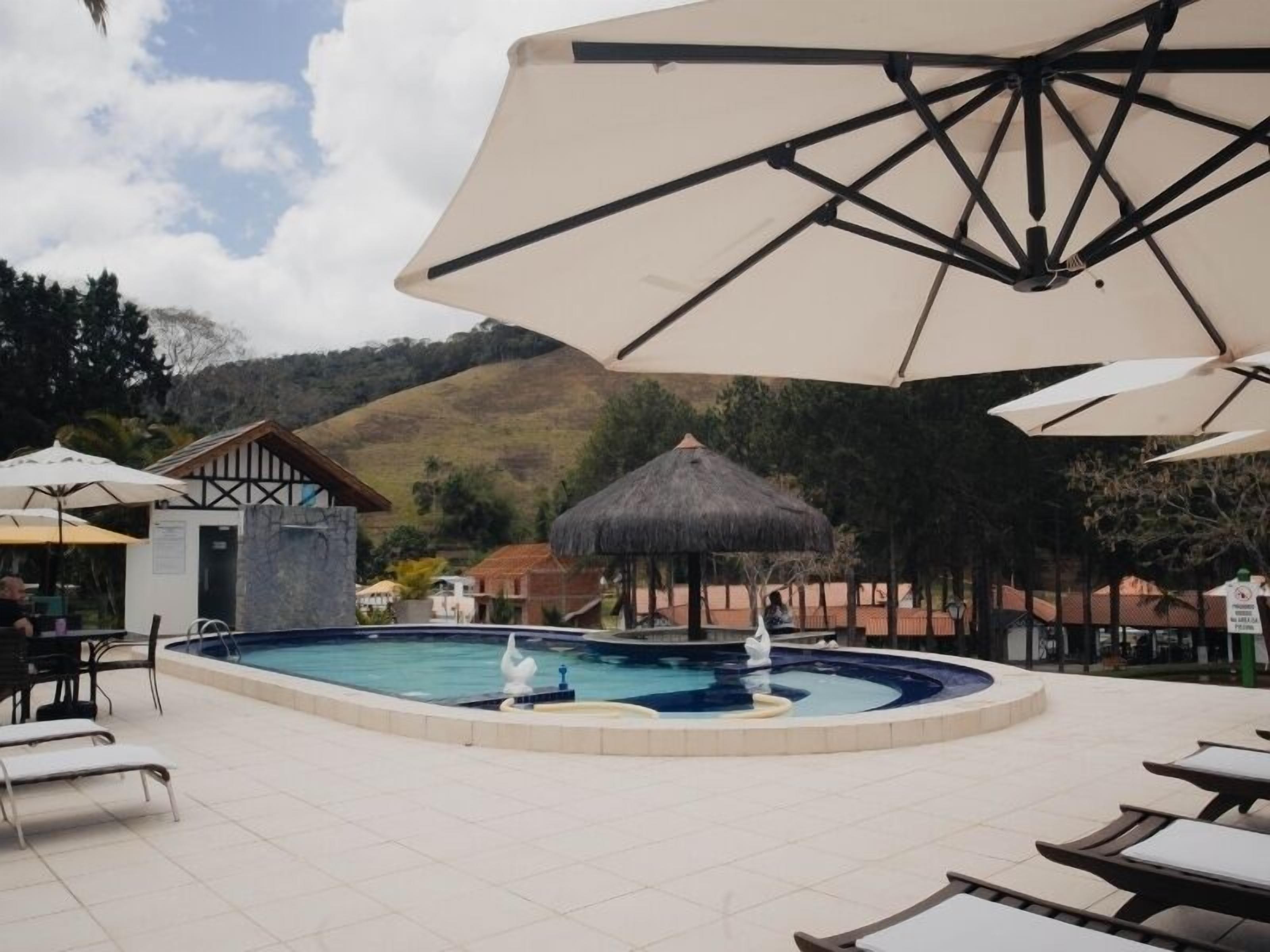 A pool area with lounge chairs, umbrellas, and a thatched-roof structure.