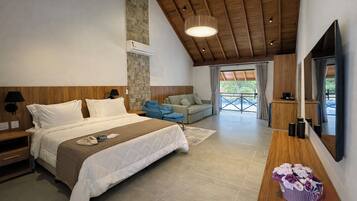 Un dormitorio moderno con una cama grande, techo de madera, pared de piedra, un sofá y un televisor.