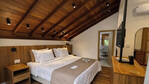 A bedroom with a wooden ceiling, a bed with white bedding, a bedside table, a nightstand, a mirror, and a TV. - Pequena Suíça Hotel Boutique (Chacara)