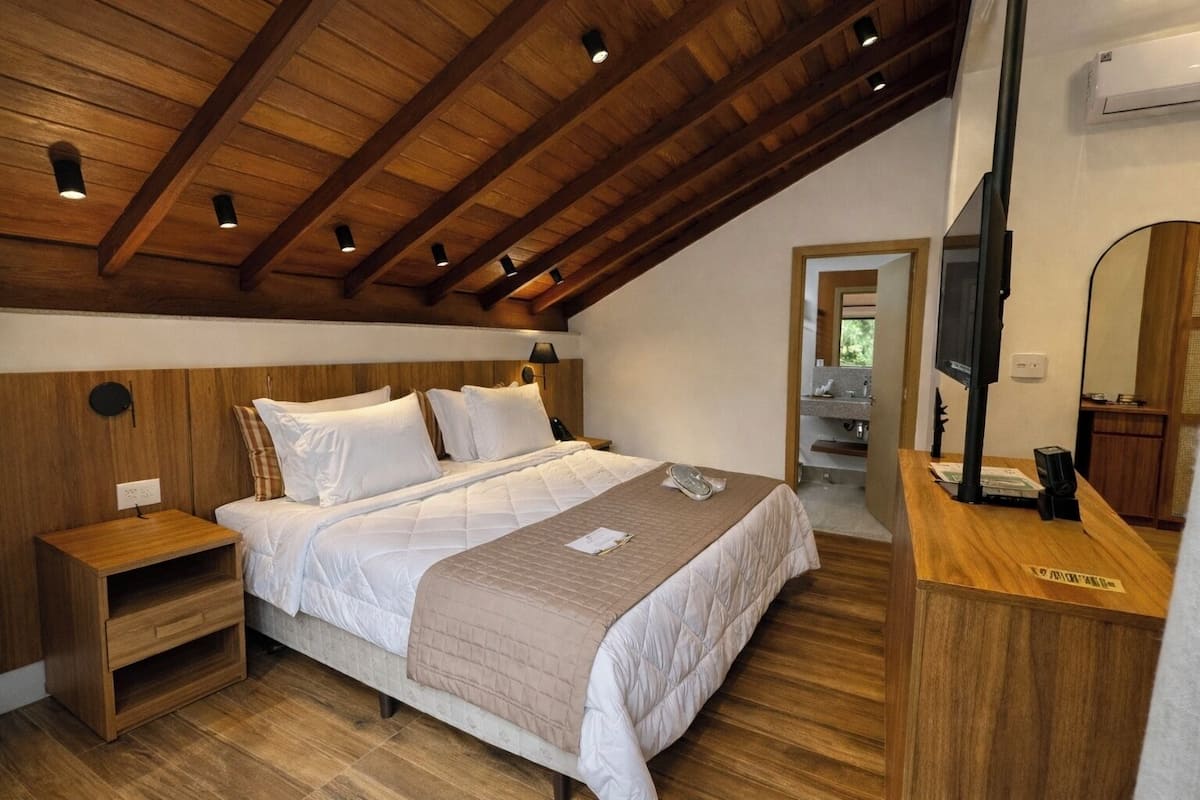Ein Schlafzimmer mit Holzbalkendecke, einem Bett mit weißer Bettwäsche, einem Nachttisch, einem Spiegel und einem Fernseher.