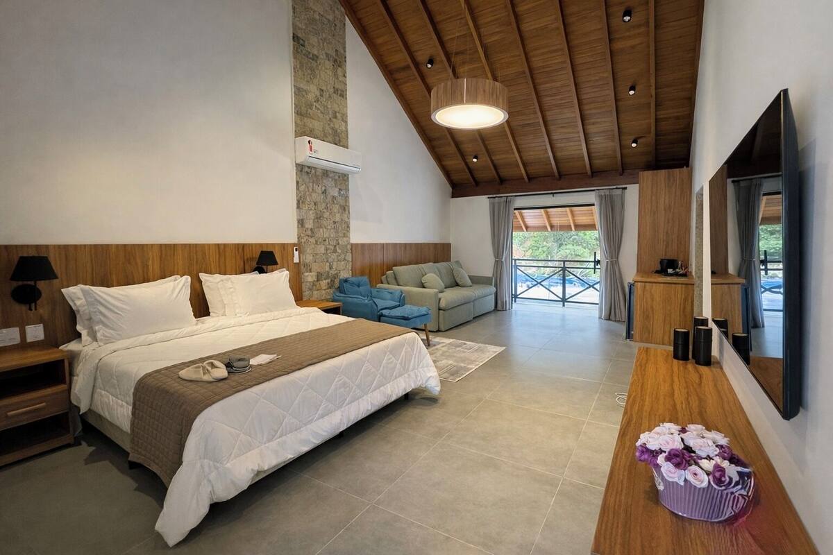 Ein modernes Schlafzimmer mit einem großen Bett, Holzboden, Steinwand, einer Couch und einem Fernseher.