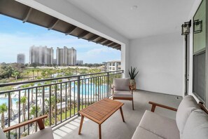 Un balcón con vista a la piscina, un sofá, una mesa y una planta en maceta.