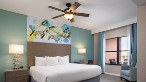 Ein Hotelzimmer mit einem großen Bett, zwei Nachttischen mit Lampen, einem Deckenventilator, einem großen Fenster mit Vorhängen und einem Sessel.