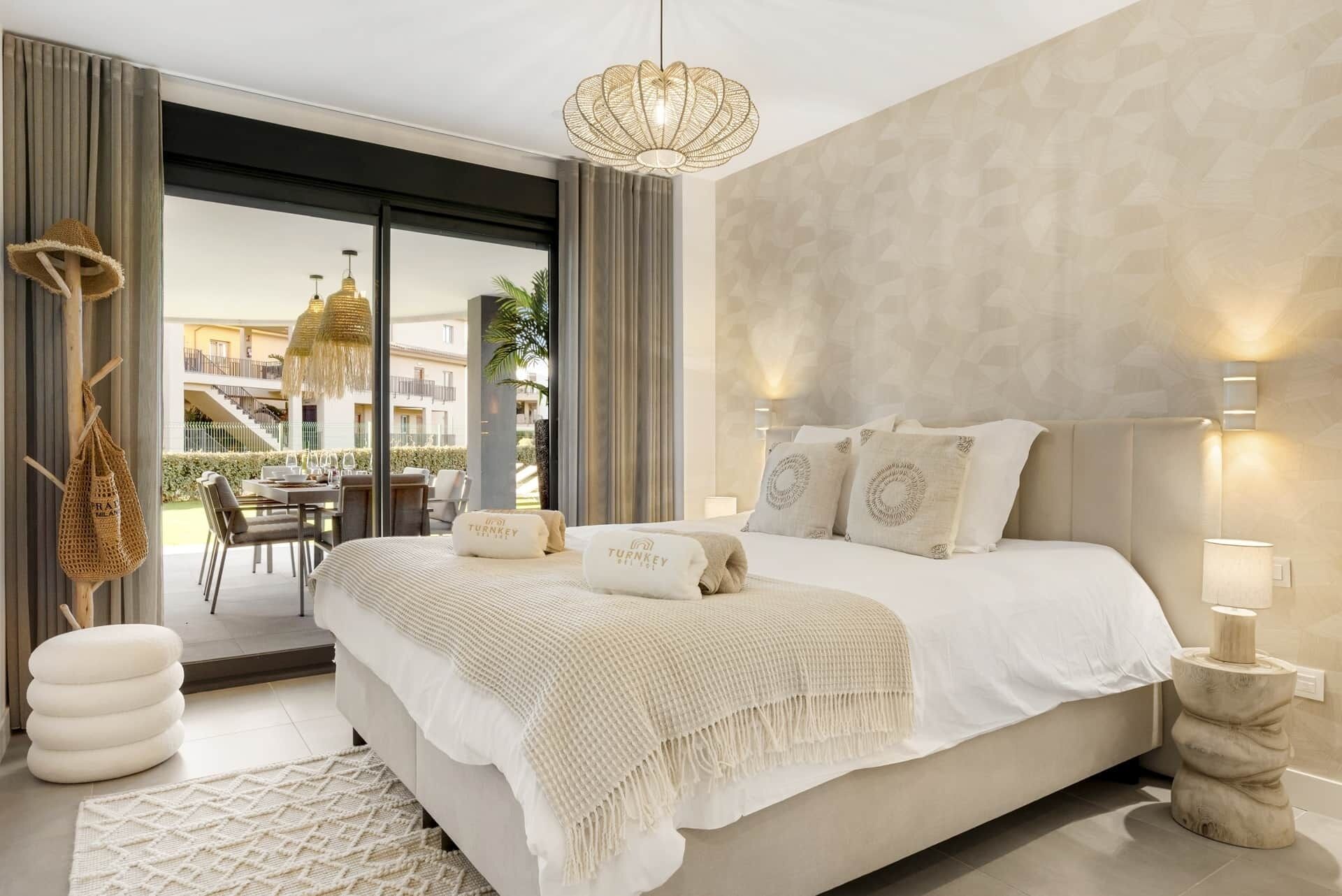A modern bedroom with a large bed, a hanging light fixture, and a view of an outdoor terrace.