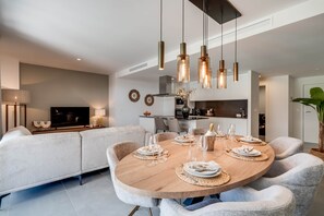 A modern dining area with a round wooden table set for six, surrounded by upholstered chairs. - Luxury 3BR Apartment with Private Terrace (Estepona)