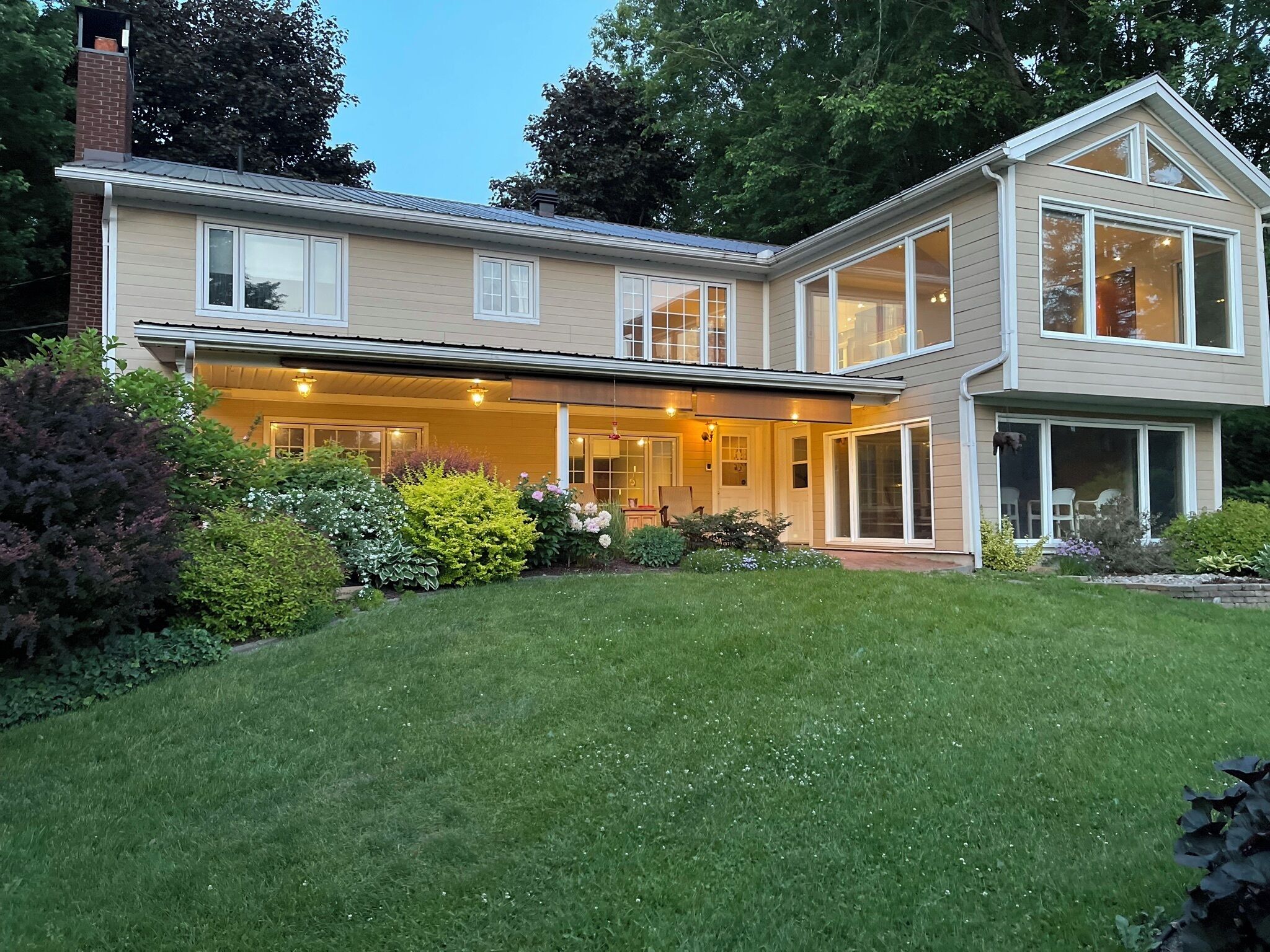 Une maison à deux étages dotée d’un patio couvert, de grandes fenêtres et d’une pelouse bien entretenue.