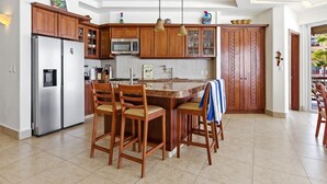 A kitchen with wooden cabinets, a stainless steel refrigerator, a microwave, and a dining area with chairs. - Four bedroom, ocean front, Vivo Resorts, Palmarito (Bajos de Chila)