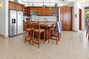 Cocina con armarios de madera, refrigerador de acero inoxidable, microondas y comedor con sillas.