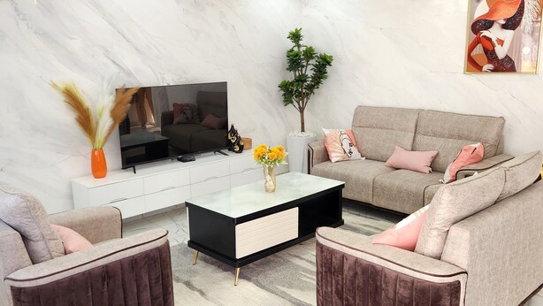 A modern living room with a marble floor, a flat-screen TV, a coffee table, two sofas, and a decorative plant. - Luxury villa (Douala)