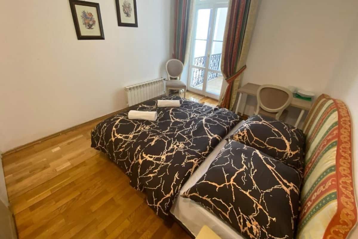 A bedroom with a bed, a chair, a radiator, and a window with curtains.