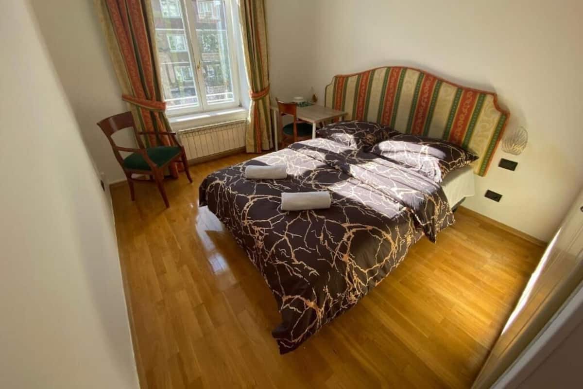A bedroom with a bed, a chair, a table, and a window with curtains.