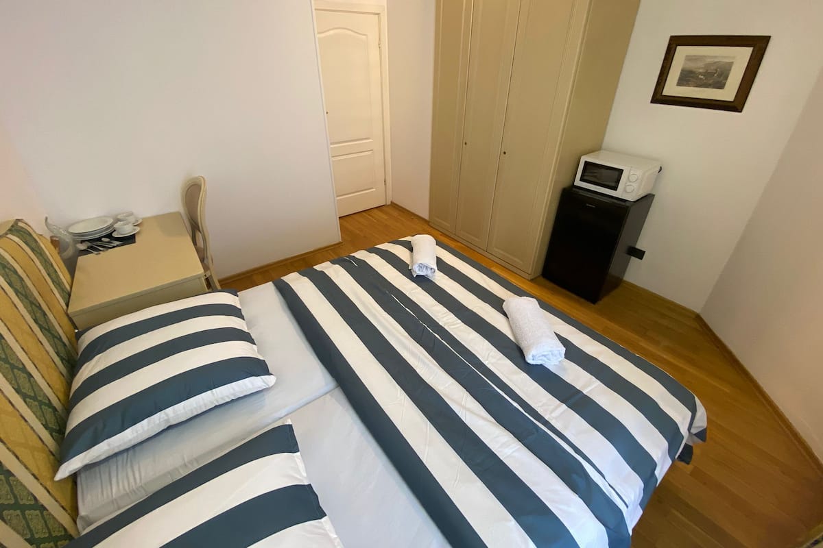 A hotel room with a bed, a small table with a chair, a microwave, and a door.