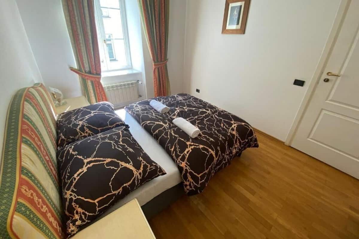A bedroom with a double bed, striped curtains, a framed picture on the wall, and a wooden floor.