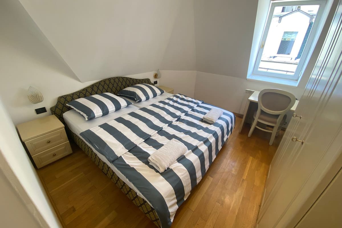 A bedroom with a bed, bedside table, chair, and a window.