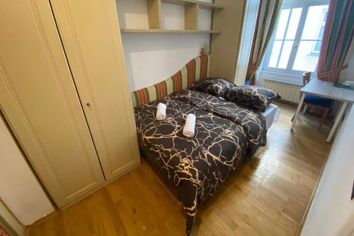 A bedroom with a bed, wooden floor, and a window with curtains.