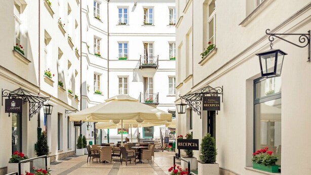 Un patio de hotel con mobiliario exterior, una zona de recepción y una escalera que conduce a la entrada.