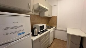Una cocina compacta con microondas, hervidor de agua y lavamanos. Se ve un refrigerador a la izquierda, y hay una encimera con un hervidor.