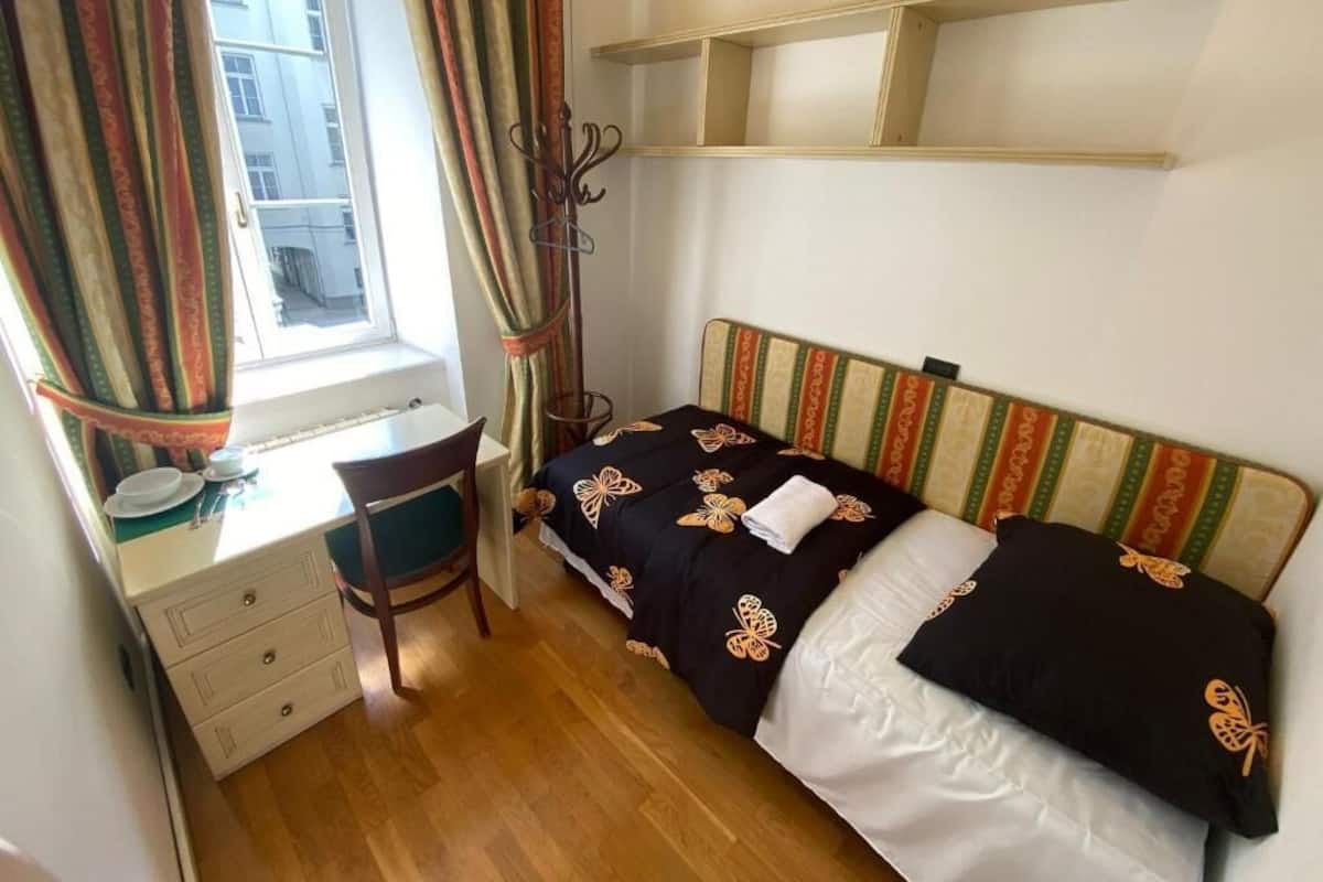 A small, tidy room with a bed, a desk, and a window with curtains.