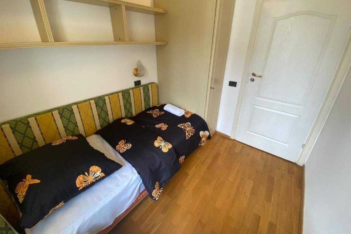 A small, single-bed room with a wooden floor, a white door, and a bed with a black and orange butterfly-patterned bedspread.