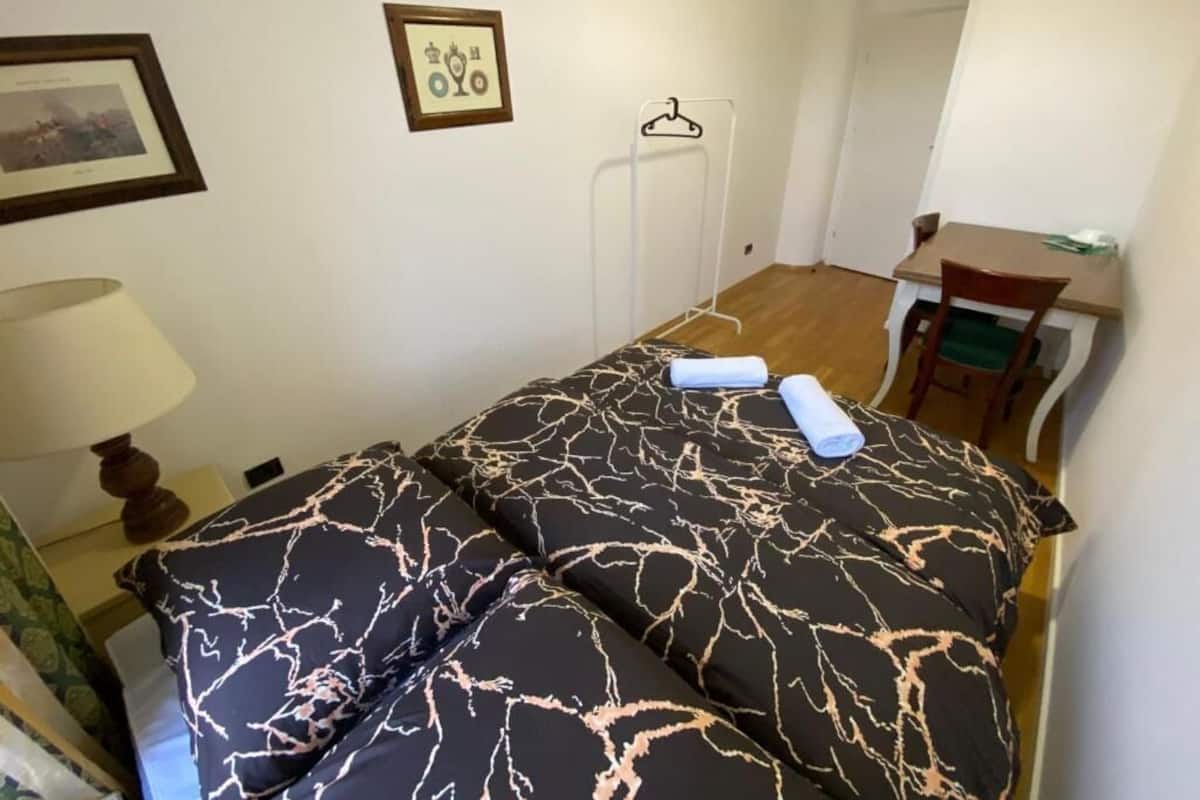 A small, neatly arranged room with a bed, a chair, a table, and a hanging clothes rack.