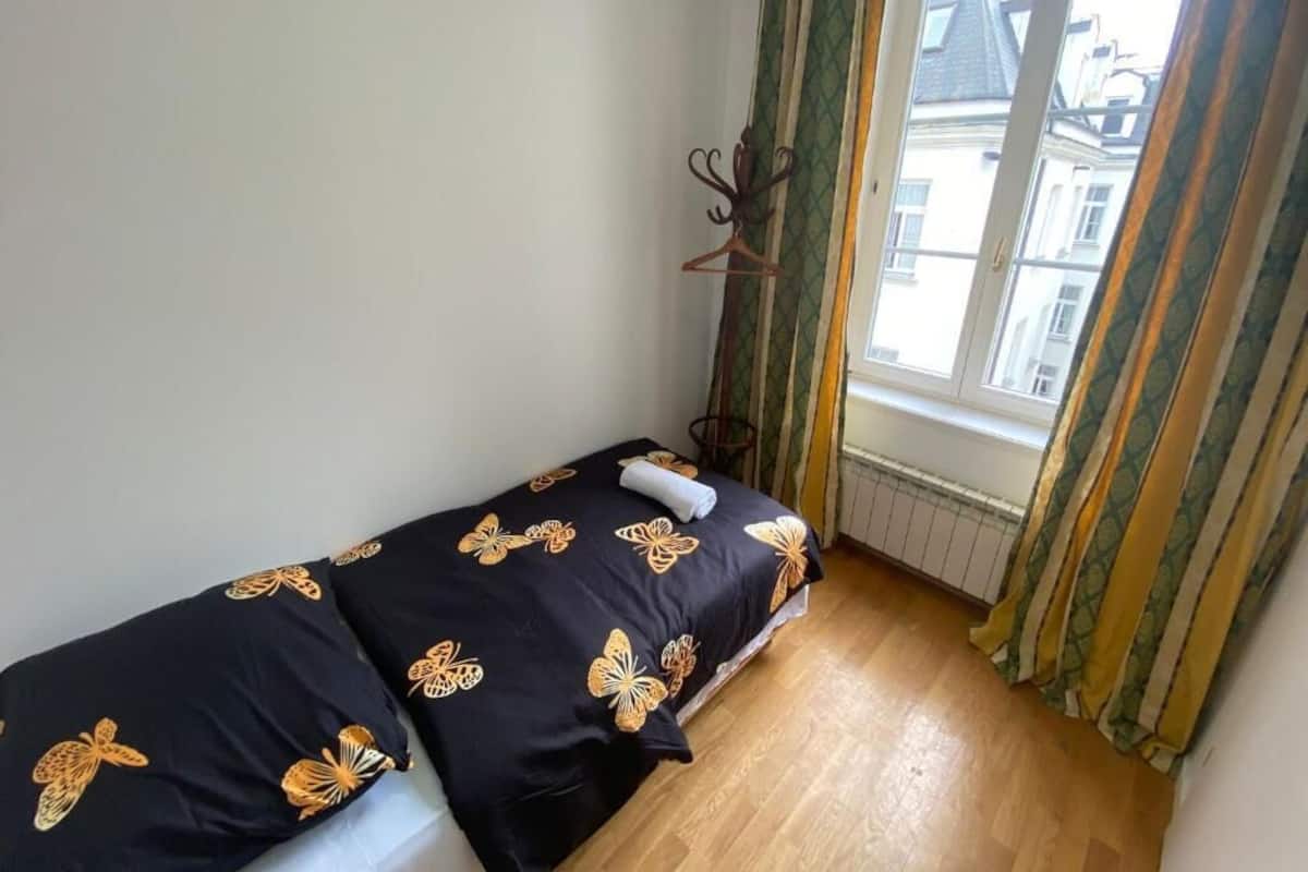 A small, single-bed room with a window, a radiator, and a wooden floor.
