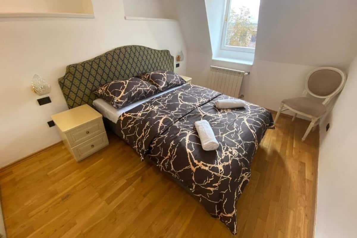 A bedroom with a bed, a nightstand, a chair, and a window.