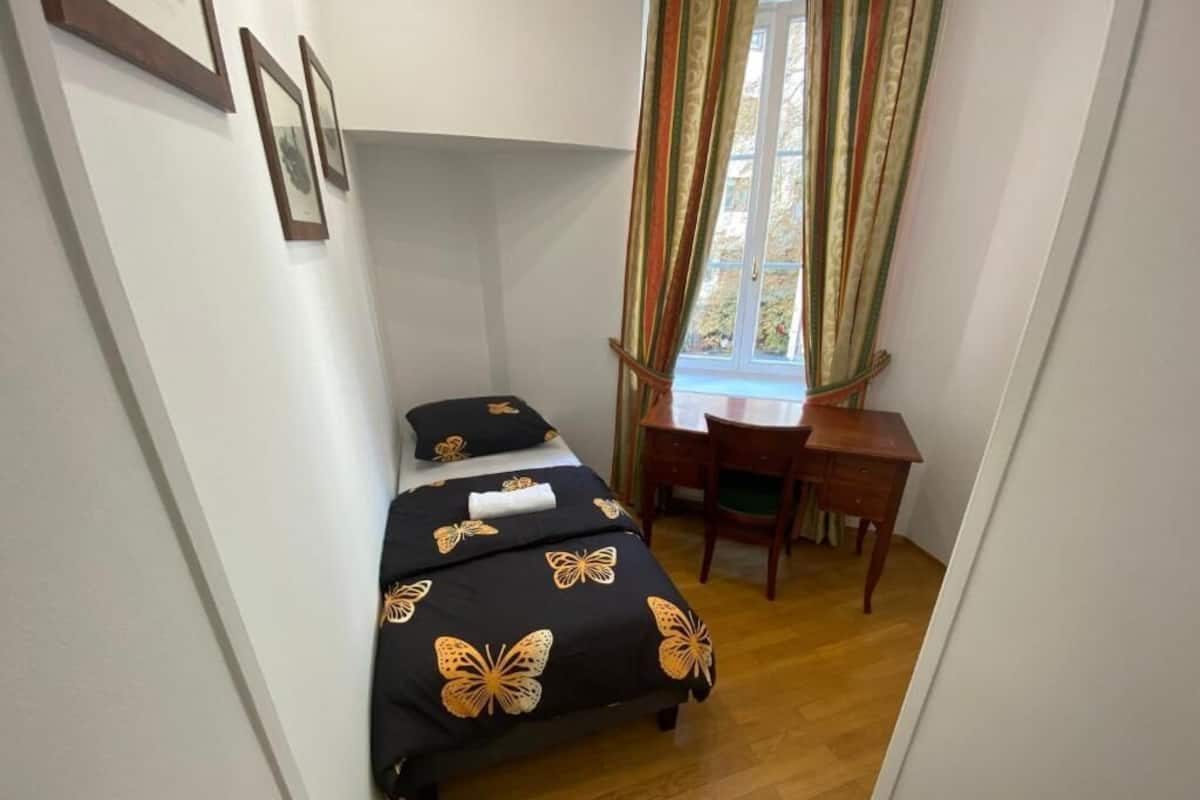 A small room with a bed, a desk, and a window with curtains.