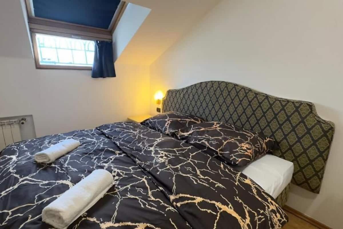 A bedroom with a bed, a nightstand, a window, and a radiator.